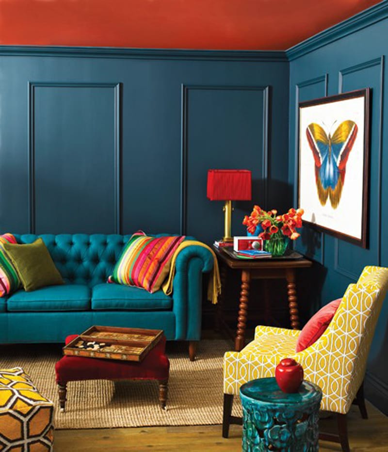 Wohnzimmer gestalten mit blauen Wänden und roter Decke-Sofa blau mit farbigen Sofadecken-polstersessel gelb-kleinmöbel aus Holz