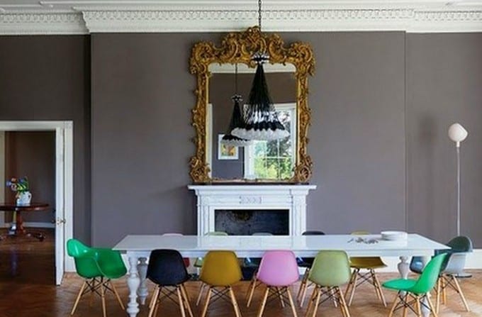 farbgestaltung wohnzimmer in grau-graue wand mit weißem kamin und Wandspiegel mit goldenem Rahmen-weiße Holztisch mit farbigen Stühlen