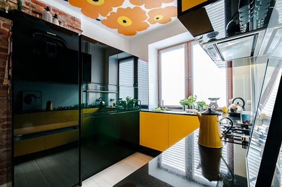 ideen für moderne küche mit schwarzen küchenschränken, schwarzer küchenarbeitsplatte über gelben unterschränken und ziegelwand