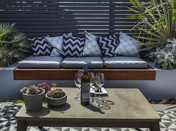 coole gartenideen für moderne gartengestaltung mit betoncouchtisch, ausgemauerter sitzbank mit hochbeeten, hochbholzsitz und grauen polstern,mosaikbodenbelag mit geometriefiguren in schwarz und gartenzaun grau